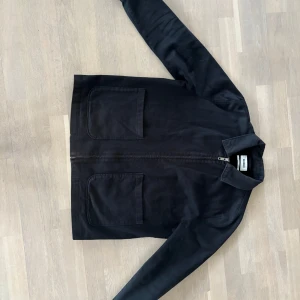 Svart jacka från Weekday - Säljer en stilren svart jacka från Weekday i storlek L. Jackan har en dragkedja framtill och två stora fickor. Perfekt för en minimalistisk look.