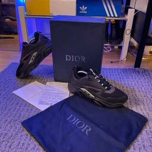 Svarta sneakers från Dior - Snygga svarta sneakers från Dior med reflekterande detaljer. Skorna har en modern design med snörning och en robust sula. Perfekta för dig som vill ha en stilren look med en touch av lyx.