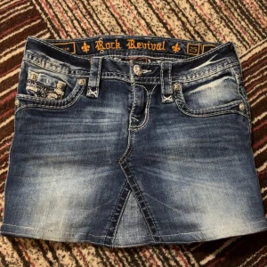 Blå reworked jeanskjol från Rock Revival - Snygg blå jeanskjol från Rock Revival med slitna detaljer och dekorativa bakfickor. Midjemått: 39cm. Jag köpte den för typ mer än 500kr från benim denim 