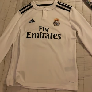 Vit långärmad fotbollströja från Adidas - Säljer en vit långärmad fotbollströja från Adidas med Real Madrids emblem och Fly Emirates-tryck. Tröjan har svarta ränder på axlarna och är tillverkad i Climalite-material för optimal komfort. Även äkta alla tröjor som säljs är äkta! Pruta gärna 👍🏼