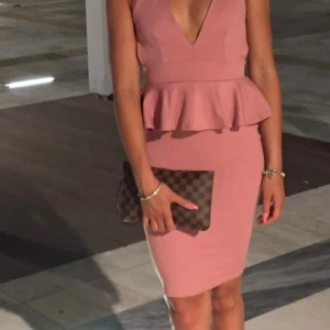 Rosa klänning från Boohoo - Snygg rosa klänning från Boohoo med volangdetalj i midjan och djup v-ringning. Klänningen har en tight passform och är ärmlös med smala axelband. Perfekt för en kväll ute eller en speciell tillställning.