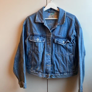 Blå jeansjacka från Amisu - Säljer en klassisk blå jeansjacka från Amisu. Jackan har en normal passform med knappar framtill och två bröstfickor med knappstängning. 