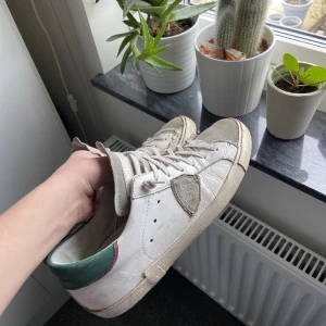 Vita sneakers från Philippe Model - Säljer ett par vita sneakers från Philippe Model med grå detaljer och gröna sulor. Skorna har snörning och en klassisk design som passar till många stilar.