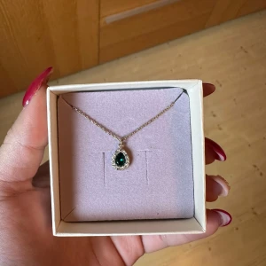 Halsband från Lily and Rose - Elegant halsband från Lily and Rose. Halsbandet är en droppformad grön sten omgiven av gnistrande klara stenar. Perfekt för studenten, bröllop, fester och bal. Säljer halsbandet och örhängen separat.