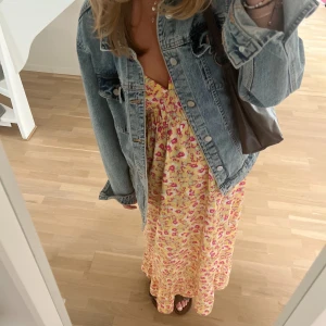 Blommig långklänning med v-ringning - Säljer en somrig långklänning i gult med blommigt mönster i rosa och rött. Klänningen har en v-ringning bak och fram så med öppenrygg och korta ärmar, perfekt middsommar klänning!! Säljer pgd att den inte kommer till användning. (Är 175 cm) Använd en gång🥰🌸