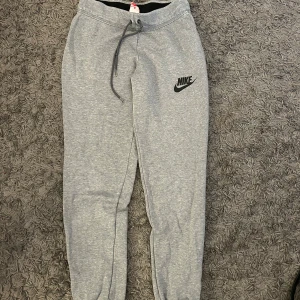 Grå mjukisbyxor från Nike - Säljer ett par grå mjukisbyxor från Nike med elastisk midja och dragsko. Byxorna har en avslappnad passform och är perfekta för en chill dag. Nike-loggan är tryckt på vänster ben.