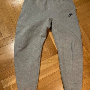 Grå mjukisbyxor från Nike - Säljer ett par grå mjukisbyxor från Nike. De har en elastisk midja och en liten Nike-logga på vänster ben. Perfekta för en avslappnad stil.