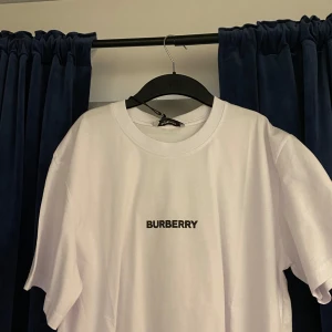 Vit t-shirt från Burberry - Snygg vit t-shirt från Burberry med svart logotyp på framsidan och ett stort grafiskt mönster på baksidan. Perfekt för en stilren och modern look. Aldrig använd , pris lapp o allt sitter på nypris 390 EUR. Pris kan diskutera 