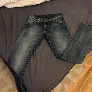 Blå jeans från Nudie Jeans - Säljer ett par snygga blå jeans från Nudie Jeans. De har en klassisk femficksdesign med märkets ikoniska broderi på bakfickorna. Jeansen har en dragkedja och knapp i midjan.