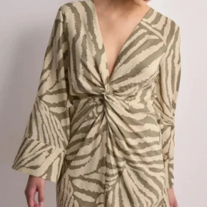 Beige och vit zebramönstrad klänning från JDY! Oanvänd!  - Snygg zebramönstrad klänning från JDY med v-ringning och knytning framtill. Klänningen har långa ärmar och en kort längd, perfekt för en trendig look. Färgen heter Färg: Tapioca Mermaid Zebra. Lånade bilder fr NellyVida ärmar Djup v-ringning Knutdetalj Kort modell.    Nyskick!!! Fler bilder finns! 