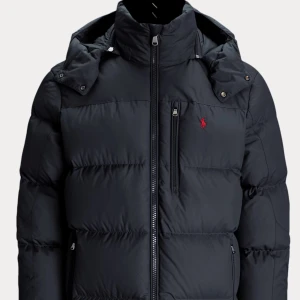 Mörkblå dunjacka från Ralph Lauren - Snygg mörkblå dunjacka från Ralph Lauren med dragkedja och huva. Jackan har en liten röd logotyp på bröstet och praktiska fickor med dragkedja. Perfekt för kyliga dagar. Inga defekter eller liknande, köpt för cirka 4000 