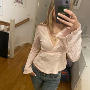 Rosa omlottopp från Gina Tricot - Säljer en söt rosa omlottopp från Gina Tricot. Toppen har långa ärmar och ett knytband i midjan för en fin passform. Perfekt för en stilren look.