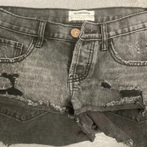 Grå jeansshorts från One X One Teaspoon - Snygga grå jeansshorts strl 29 med slitna detaljer och fransiga kanter. De har en knappar som man knäpper. Perfekta för en avslappnad stil. Säljer då dom va förstora❤️Därav aldrig använda, skriv för fler bilder eller ev frågor❤️