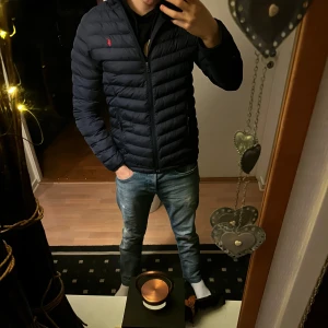 Mörkblå pufferjacka från Polo Ralph Lauren - Säljer en snygg mörkblå pufferjacka från Polo Ralph Lauren. Jackan har en dragkedja framtill och två praktiska fickor med dragkedjor. Den är perfekt för kyligare dagar och har en stilren design med det klassiska Polo-logotypen på bröstet. En dragkedja sönder 