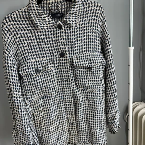 Rutig jacka från Zara - Snygg rutig jacka från Zara i svart, vit och blå. Jackan har en klassisk krage och knappar framtill. Två fickor med lock på bröstet ger en cool touch. Perfekt för att lyfta din outfit! Ena bröstfickan är trasig men går lätt att sy för den händige.