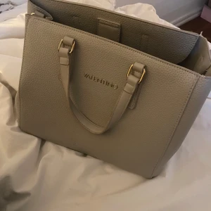 Beige handväska från Valentino - Valentino väska som inte kommer t användning längre! Jättefin men har några skavanker där handtaget sitter fast och inuti men inget man tänker på. Köpt på plick förra året och kommer med ett långt band💖 skriv gärna innan du köper och för frågar! diskuterar gärna priset 