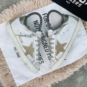 Vita sneakers med stjärndetalj - Snygga vita sneakers från Golden Goose med en glittrig stjärna på sidan. Skorna har snörning och en klassisk design med en touch av glamour. Perfekta för en trendig look.