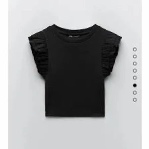 Svart croppad topp med volangärmar - Snygg svart croppad topp med volangdetaljer på ärmarna. Perfekt för en trendig look. Passar bra till jeans eller kjol.