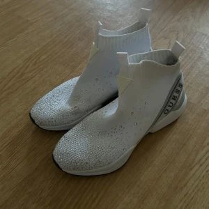 Vita sneakers med glittrig design - Snygga vita sneakers med en glittrig ovandel och ribbad kant. Skorna har en modern design med textdetalj på hälen och är perfekta för att ge din outfit en extra touch. Endast använda 1 gång 😊