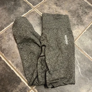 Grå leggings från Gymshark - Säljer ett par grå leggings från Gymshark. De är perfekta för träning med sin tighta passform och bekväma material. Leggingsen har en diskret logga på sidan och är designade för att ge bra stöd under träningspasset. De är väl använda men har inga skador eller liknade vad jag sett