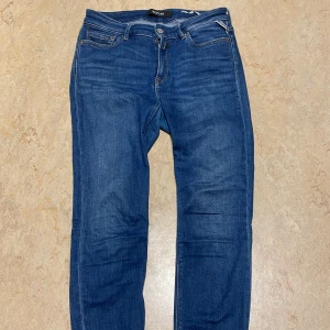 Blå jeans från Replay - Snygga blå jeans från Replay med klassisk femficksdesign och knappgylf. Perfekta för en avslappnad stil. De har en normal passform och är tillverkade i slitstarkt denim. Storlek 28
