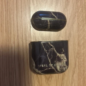 Ideal of Sweden AirPods fodral - Snyggt AirPods fodral i svart med marmorerat mönster och gulddetaljer från Ideal of Sweden. Fodralet har en elegant design som skyddar dina hörlurar med stil.💗