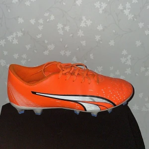 Orange fotbollsskor från Puma , inte använda så mycket  - Säljer ett par orange fotbollsskor från Puma med snörning och vita detaljer. Skorna har en lätt och smidig design med dobbar för bra grepp på planen. Perfekta för fotbollsspelare som vill sticka ut på planen.