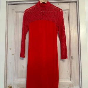 Röd spetsklänning - Snygg röd klänning med spetsdetaljer och långärmad design. Perfekt för en elegant look med hög hals och figurnära passform. Klänningen har en vacker spetsöverdel som ger en romantisk touch.
