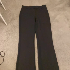 Mörk gråa byxor från Nelly - Snygga mörkgråa byxor från Nelly i storlek S. Byxorna har en klassisk bootcut-stil och är perfekta för en stilren look. De är tillverkade i ett mjukt material och har en knappdetalj i midjan. Stretchigt material. Har aldrig kommit till användning då dom inte passar helt!😁