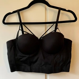 Svart korsett-topp med smala axelband - Snygg svart korsett med smala axelband och vadderade kupor. Den har en stilren design med flera hakar i ryggen för justerbar passform. Perfekt för en utekväll eller fest! 🖤