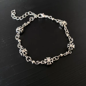 Handgjort Silverfärgat armband med korsdetaljer - Snyggt silverfärgat armband med unika korsformade detaljer. ca 15 cm och kan justeras upp till 20 cm! Armbandet har en justerbar kedja och ett smidigt lås. Perfekt för att ge en edgy touch till din outfit. Passar både till vardags och festliga tillfällen.