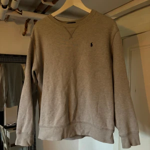 Beige tröja från Ralph Lauren - Säljer en beige tröja från Ralph Lauren. Den har en liten logga på bröstet och är i bomull. Tröjan är långärmad och har en liten reva på ärmen samt en fläck på framsidan. 