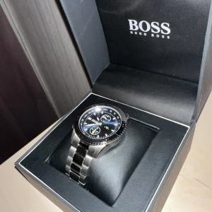 Hugo Boss klocka i silver - Säljer en stilren Hugo Boss klocka i silver med en snygg blå urtavla. Klockan har en robust metallarmband och kommer i originalförpackning. Perfekt för både vardag och fest! PRIS KAN DISKUTERAS 