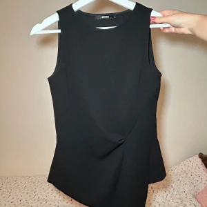 Svart ärmlös topp från bikbok - Snygg och stilren svart ärmlös topp från bikbok. Den har en enkel design med en rund halsringning och är gjord i ett bekvämt material! 