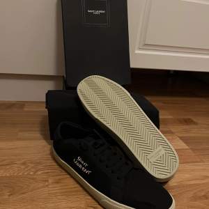 Säljer ett par stilrena svarta sneakers från Saint Laurent i mycket bra skick. Skorna har en vit sula och Saint Laurent-loggan i vitt på sidan. Perfekta för både vardag och fest! Kommer med originalkartong och dustbag. Säljer skorna då de inte passade mig. Köpte här på Plick så kan inte lämna tillbaks. Använd 2-3 gånger men 10/10 skick. Storlek 45 men sitter mer som 43-44