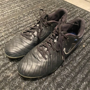 Svarta fotbollsskor från Nike - Säljer ett par svarta Nike fotbollsskor i bra skick. Skorna har snörning och en slitstark sula med dobbar, perfekt för fotbollsträning eller match. De är bekväma och ger bra grepp på planen. Passar dig som vill ha stil och funktion i ett!