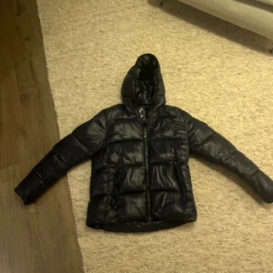 Svart pufferjacka från Save the Duck - Säljer en svart pufferjacka från Save the Duck i mycket bra skick. Det är strl M. Jackan är 100% djurfri och tillverkad med Plumtech syntetiskt dun. Den är vattenavvisande och andas bra, perfekt för höst och vinter. Har en dragkedja och en huva för extra skydd mot väder. Superbekväm och stilren! Modellen är edgard