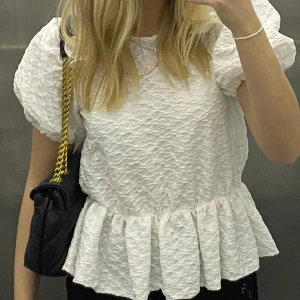Vit volang topp - Säljer en superfin vit blus med puffiga ärmar och volangdetaljer. Materialet är lätt och luftigt, vilket gör den bekväm att bära hela dagen. 