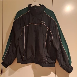 Svart och grön vindjacka från Cava Company - Säljer en cool svart och grön vindjacka från Cava Company. Jackan har en dragkedja framtill och elastiska muddar vid ärmslut och nederkant. Texten är i reflex.