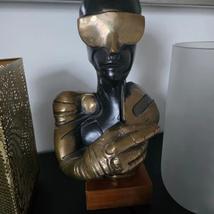 Futuristisk skulptur i guld och svart - En cool futuristisk skulptur i guld och svart. Den har en modern design med en person i hjälm och visir, vilket ger en sci-fi känsla. Perfekt som en unik inredningsdetalj för den som gillar modern konst och futuristiska teman.