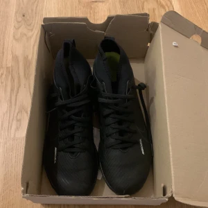 Svarta Nike Mercurial fotbollsskor - Säljer ett par svarta Nike Mercurial fotbollsskor i mycket bra skick. Skorna har en tight passform med snörning och är perfekta för inomhusfotboll. De är tillverkade i syntetmaterial och har en slitstark sula för bra grepp på planen.