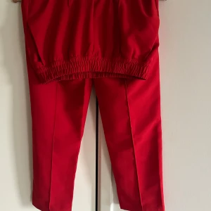 Röda byxor med resår - Snygga röda byxor i syntetmaterial med resår i midjan och vid bensluten samt två sidfickor. Perfekta för en avslappnad stil eller en färgglad touch till din outfit. De har en normal passform och är superbekväma att bära. Passar perfekt för höst och vår!