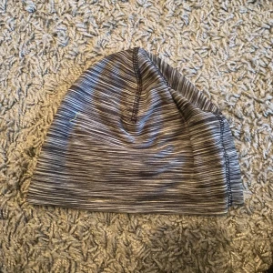 Grå randig mössa - Säljer en stilren grå mössa med randigt mönster. Perfekt för kyliga dagar och passar till de flesta outfits. Mössan är mjuk och bekväm, idealisk för både höst och vinter.