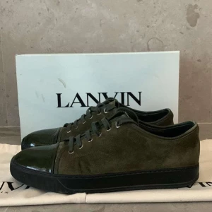 Gröna sneakers från Lanvin - Säljer ett par snygga gröna sneakers från Lanvin i bra skick, lite defekt och slitning på cap toe. Skorna har en stilren design med snörning och en glansig tå i skinn. Perfekta för både vardag och fest! Kommer med originalförpackning och dustbag.