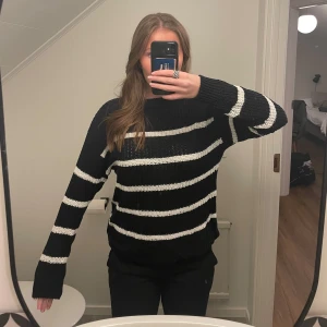 Svart och vit randig stickad tröja från 157 - Säljer en supermysig svart stickad tröja med vita ränder från 157. Den har en skön passform och är perfekt för kyliga dagar. Tröjan är långärmad och har en ribbad krage som ger extra värme. Perfekt för både vardag och mysiga hemmakvällar!