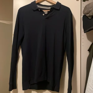 Mörkblå pikétröja från Pier One - Säljer en stilren mörkblå pikétröja från Pier One. Den har långa ärmar och en klassisk krage med knappar. Perfekt för både vardag och lite finare tillfällen. Tröjan är i bra skick och passar perfekt till höst- och vårgarderoben.  Storlek M men passar även S