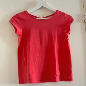Röd topp från Lindex Kids - Säljer en söt röd topp från Lindex Kids i storlek 146/152. Den har korta ärmar och en enkel design med korsade band i ryggen som ger en fin detalj. Perfekt för sommarens varma dagar! 🌞
