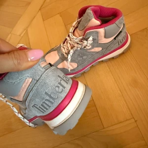Grå och rosa boots  från Timberland - Säljer ett par snygga och bekväma boots från Timberland i grått och rosa. Skorna har snörning och en robust sula med bra grepp. Perfekta för både vardag och äventyr! 🏞️