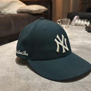 Aime Leon Dore Keps  - Snygg mörkgrön keps från Aime Leon Dore med broderad vit logga framtill och text på sidan. Perfekt för en casual look. Justerbar passform för optimal komfort.