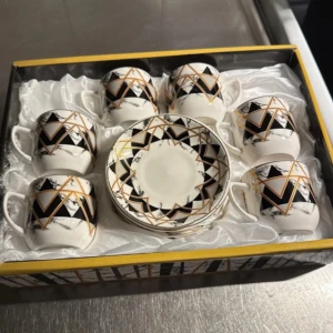 Set med espressokoppar och fat - Elegant set med sex espressokoppar och matchande fat. Designen är i svart och vitt med geometriska mönster och guldlinjer. Perfekt för att lyfta kaffestunden med en touch av stil.